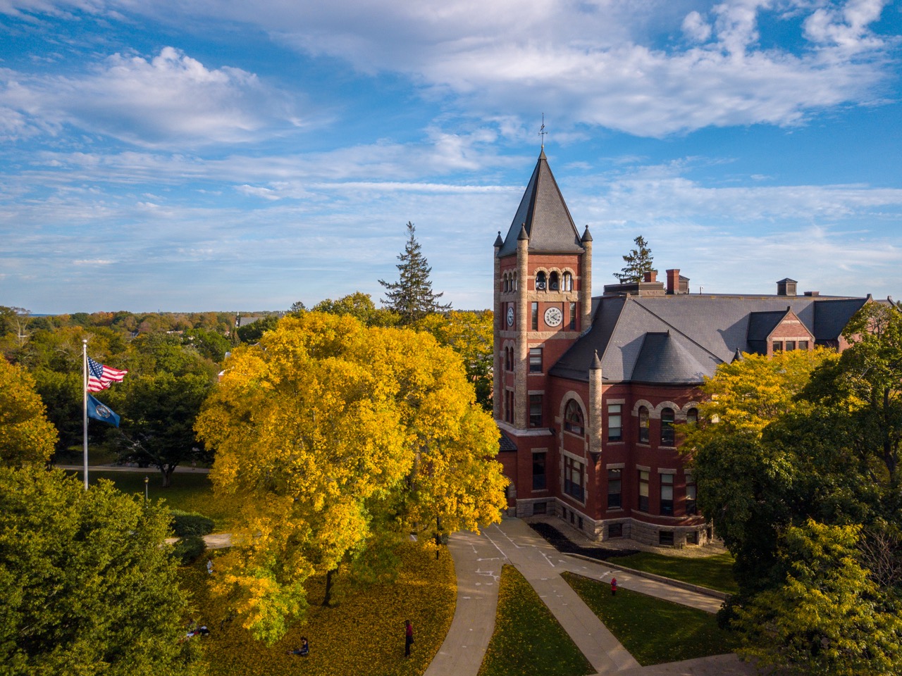 University of New Hampshire campus surrounded by yellow and trees and a bright blue sky with scattered clouds.