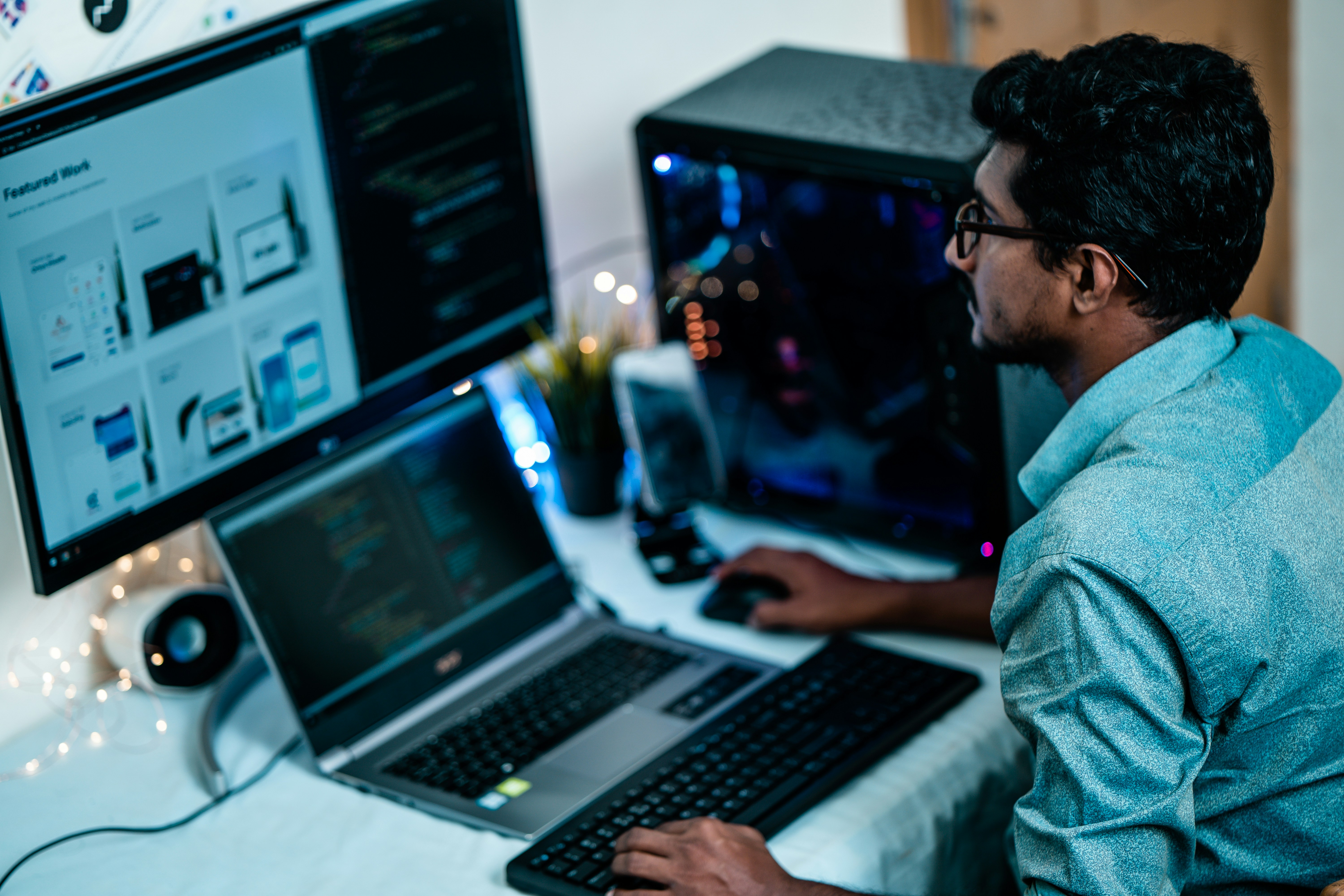 A male student sitting in front of a laptop and large monitor displaying code and design mockups.