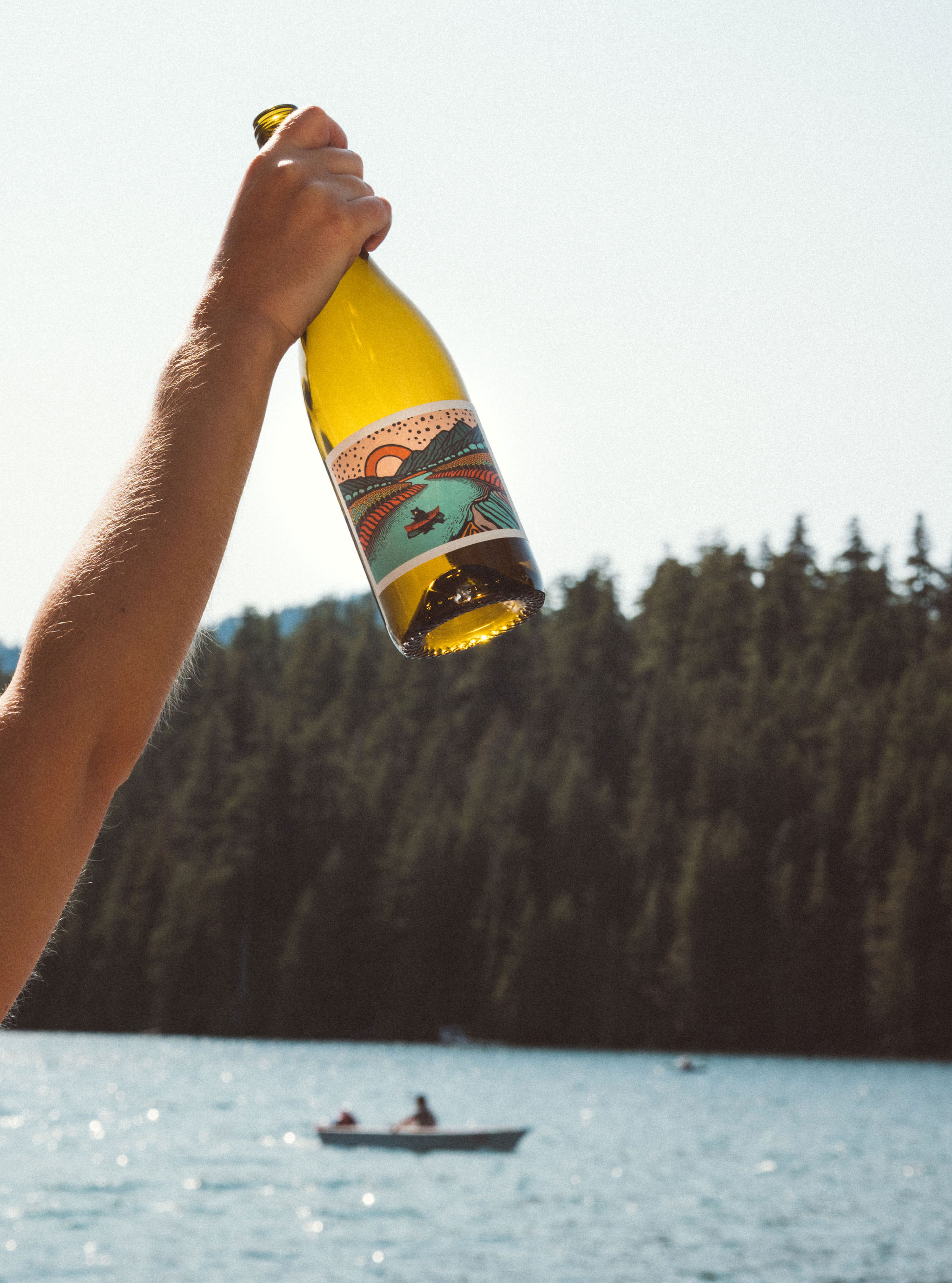 Person holding Bearboat chardonnay bottle in the air with a people in a canoe paddling in the background