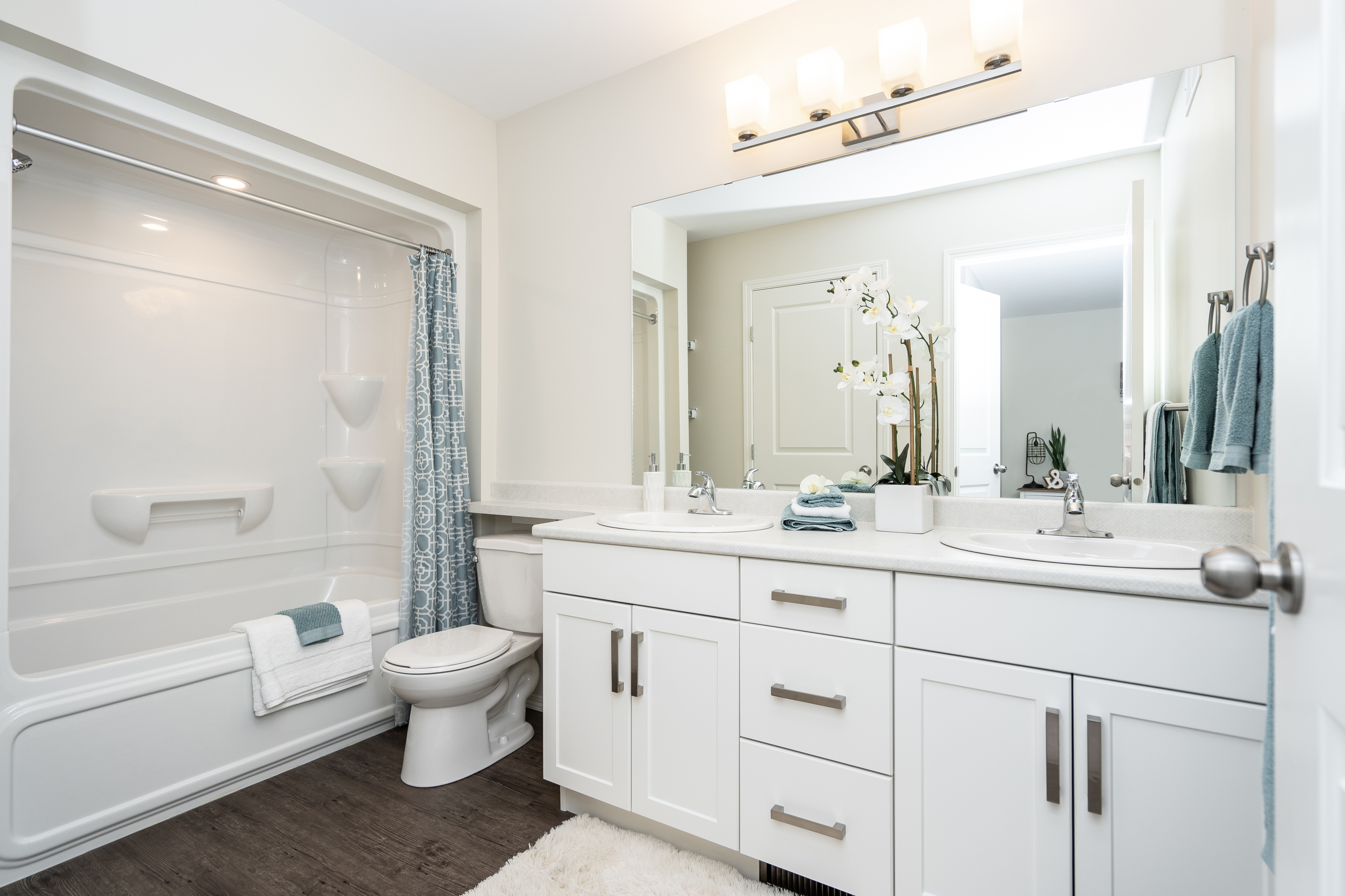 Harvest Gate bathroom with white double-sink vanity, large mirror, tub-shower combo, and modern flooring
