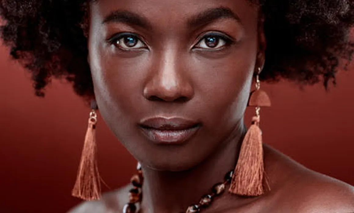 Woman with curly hair wearing long tassel earrings against red background