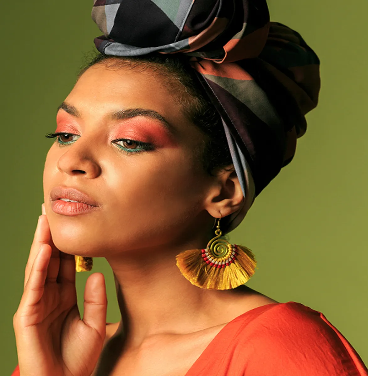 Woman with vibrant makeup, head wrap, and statement earrings posing elegantly