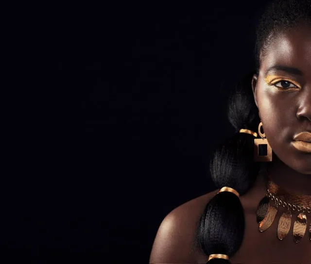 Woman with golden makeup and jewelry against dark dramatic background
