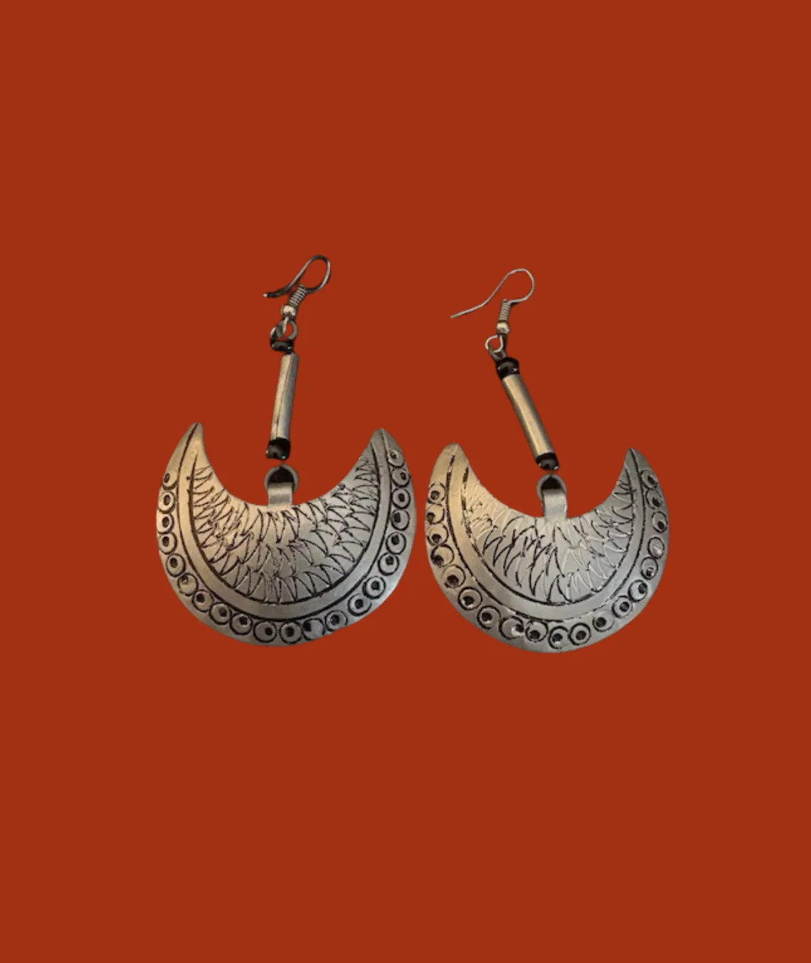 Ornate crescent moon-shaped silver earrings on rust-colored background