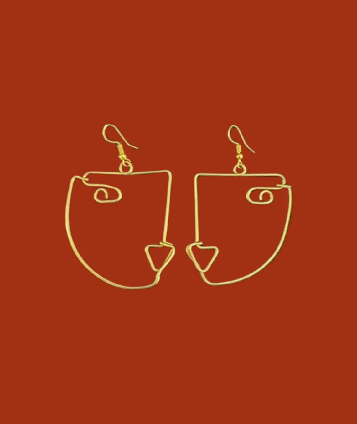 Gold wire abstract face-shaped earrings on rust-colored background