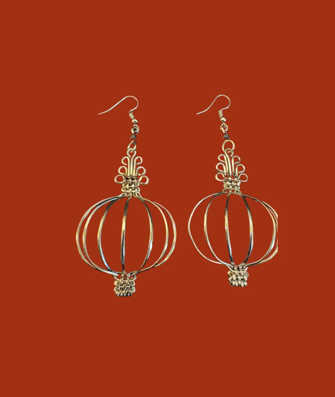 Gold wire lantern-shaped earrings against a solid red background