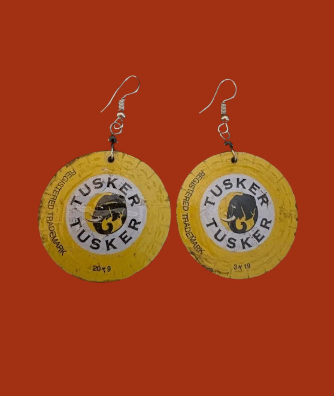 Yellow Tusker beer bottle cap earrings on red background