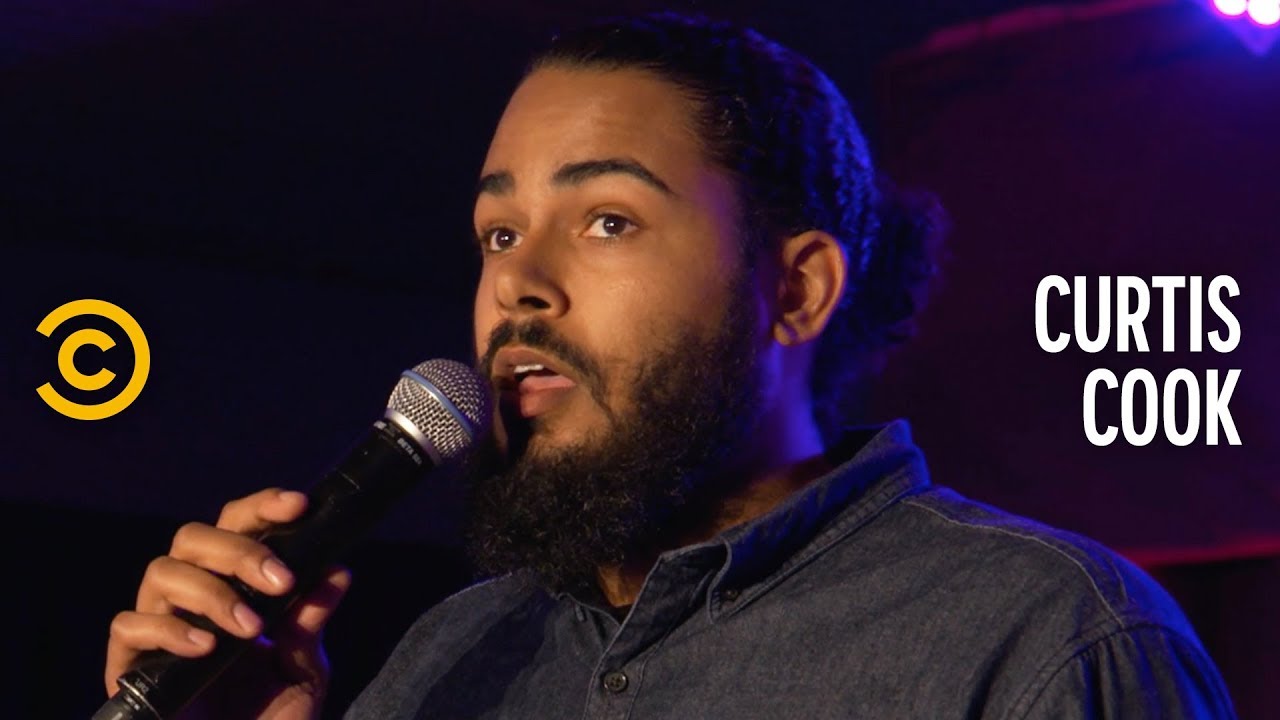 Comedian Curtis Cook speaking into a microphone with a dark background and Comedy Central logo.