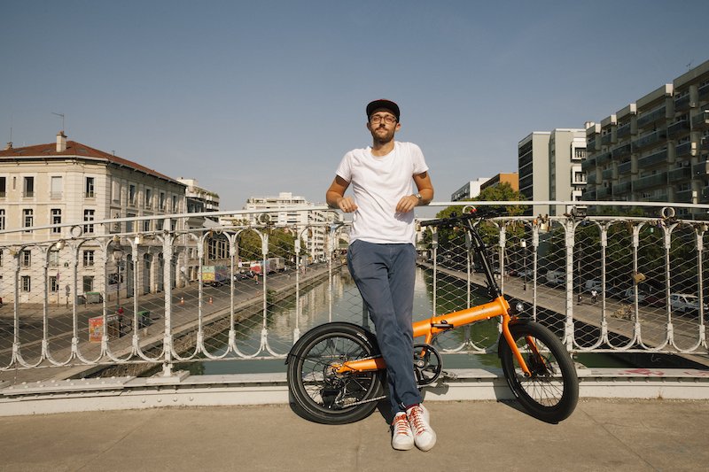 Vélotafeur qui pédale sur la route à côté d'un pont à arcs.