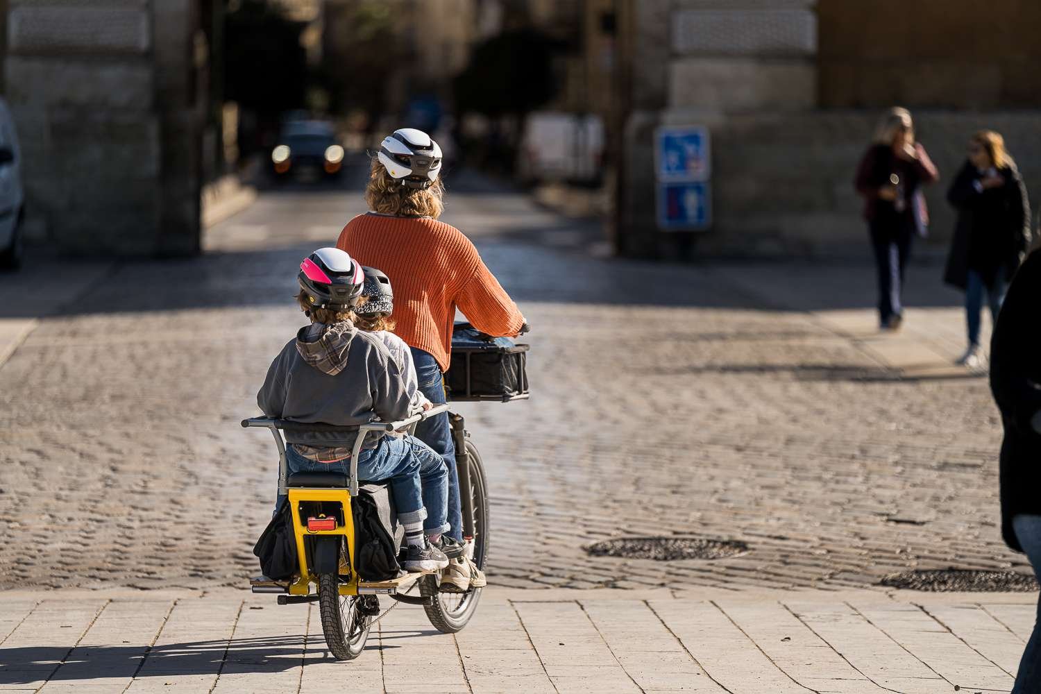Salariée transportant deux enfants en ville sur un vélo cargo Yuba Spicy Curry jaune, en location vélo entreprise