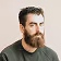Bearded man wearing a dark sweater, posing against a beige background.