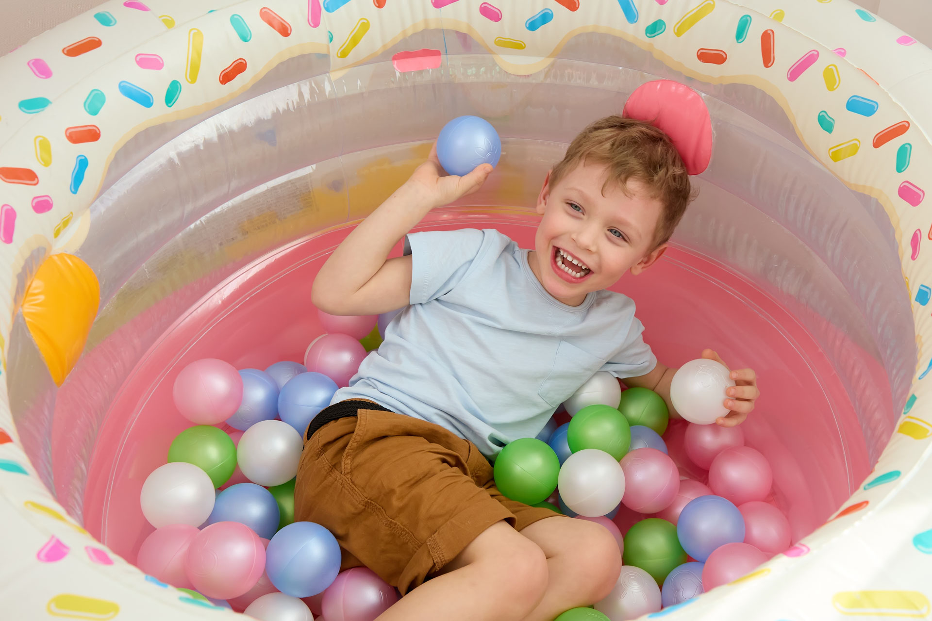 Child playing in colorful ball pit with joyful expression.