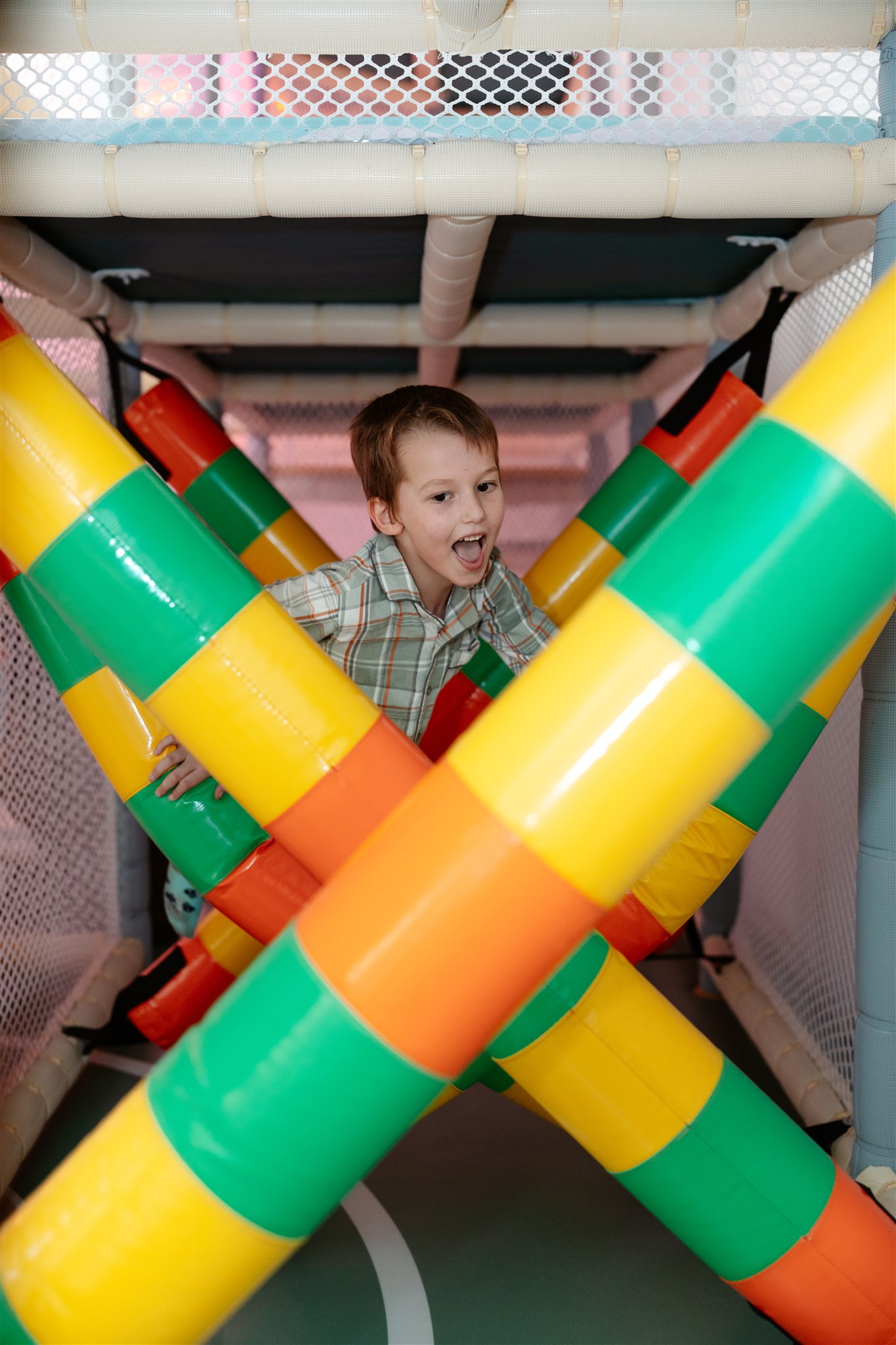 Child holding small potted plants with a playful smile against a pastel background.