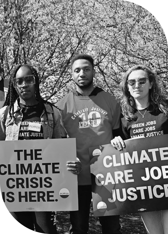 Three people standing side by side: one holding a “The climate crisis is here” placard, another wearing a “Celebrate Justice” shirt, and the third wearing a “Green Jobs” shirt while holding a “Climate Care Job Justice” placard, representing The Green New Deal Network, a collective Action Fund at Tides Foundation.