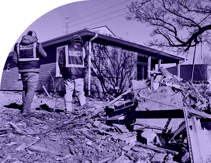 Two BeLoved Asheville volunteers walk near a home assessing storm damage after Hurricane Helene, supporting community-led disaster relief efforts.