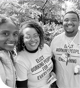 Three smiling community organizers wearing “Elect Working People for Everything” shirts, standing together outdoors in support of civic engagement and social change.