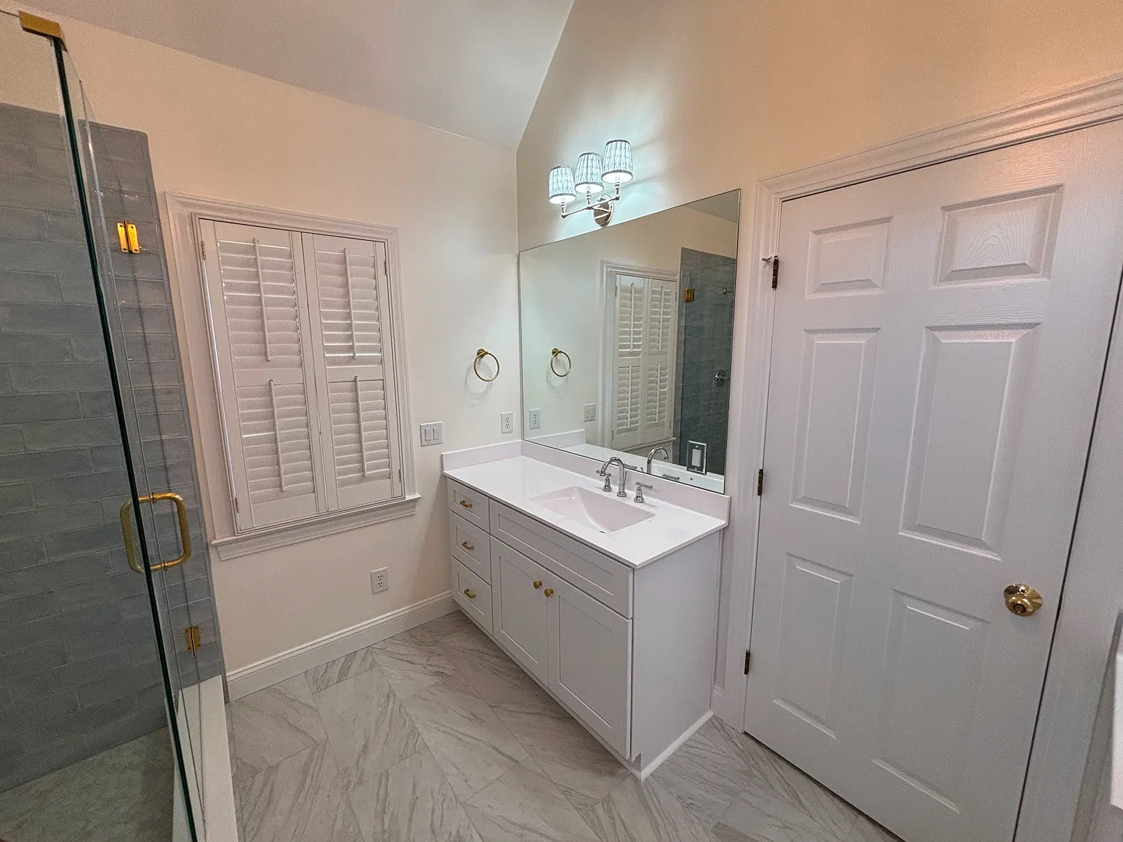Modern bathroom with white vanity, large mirror, glass shower with gray tiles, and marble floor.