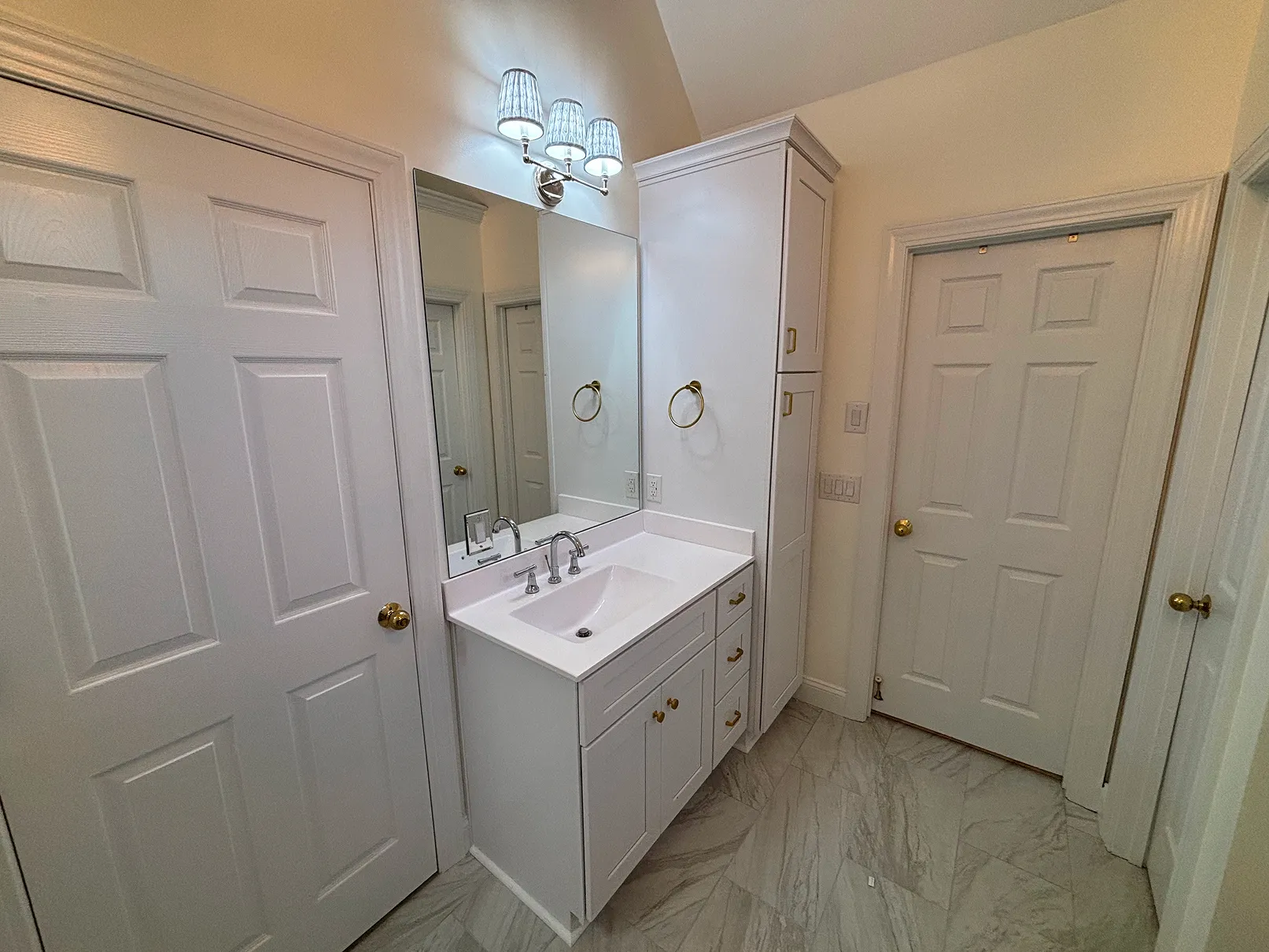 Modern bathroom vanity with white cabinetry, gold hardware, a rectangular sink, and a large mirror with three light sconces above.