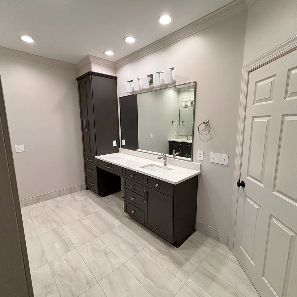 Modern bathroom vanity with dark wood cabinets, white countertop, under-mount sink, large mirror, and four-light fixture above.