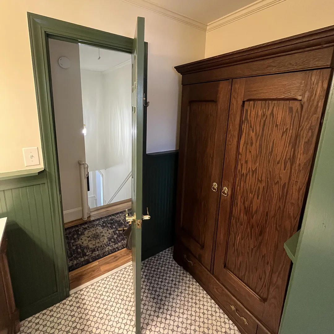 Partially open green door within a small room with patterned tile floor, green wainscoting, and a large wooden armoire.
