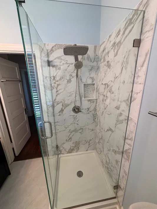 Modern shower with glass door, marble tile walls, overhead rain showerhead, and handheld shower.