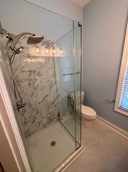 Modern bathroom with glass shower enclosure, marble tiled wall, toilet, and light blue walls.