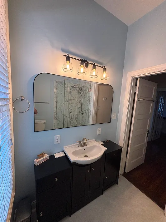 Bathroom vanity with white sink, black cabinets, large mirror, and four-light fixture above it.