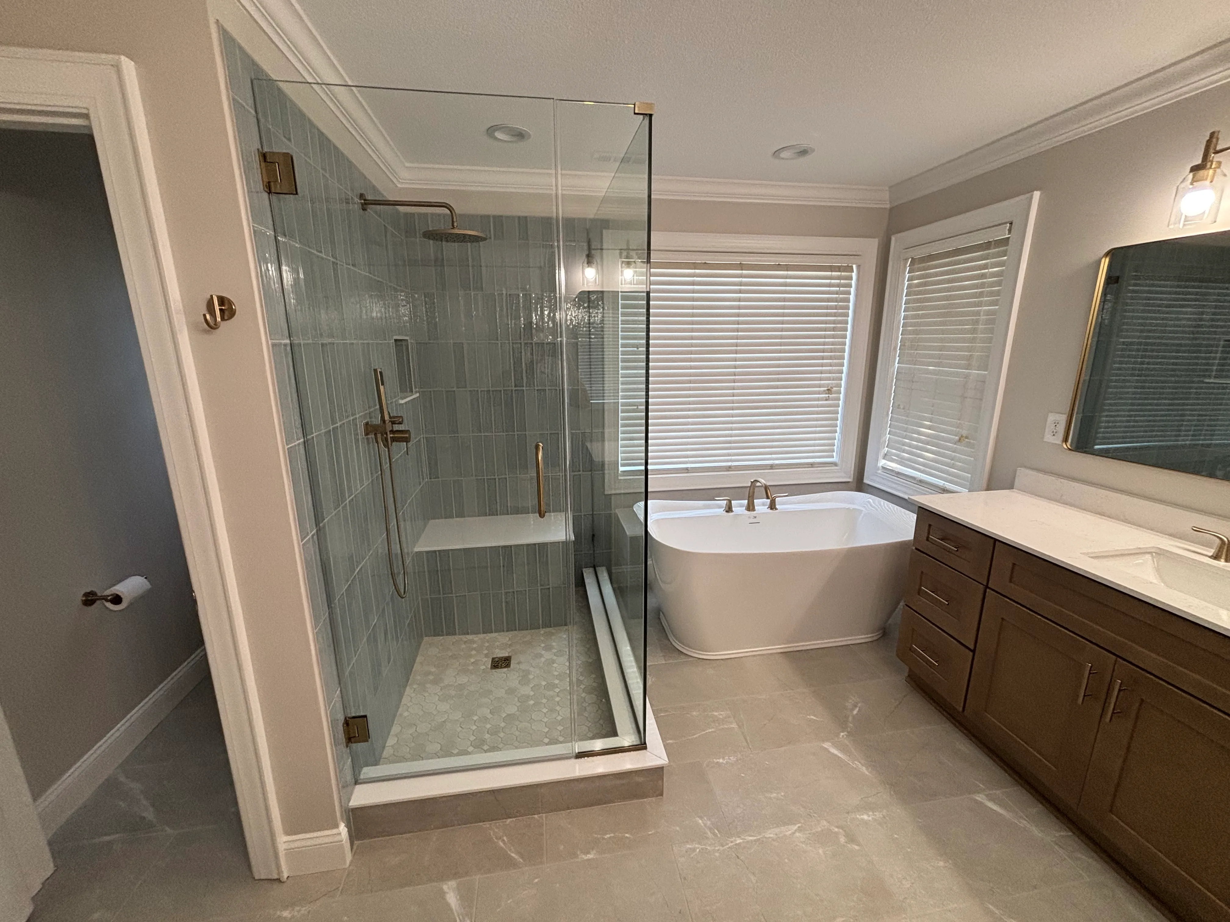 Modern bathroom with glass shower, freestanding bathtub, wooden vanity, and tiled floor.