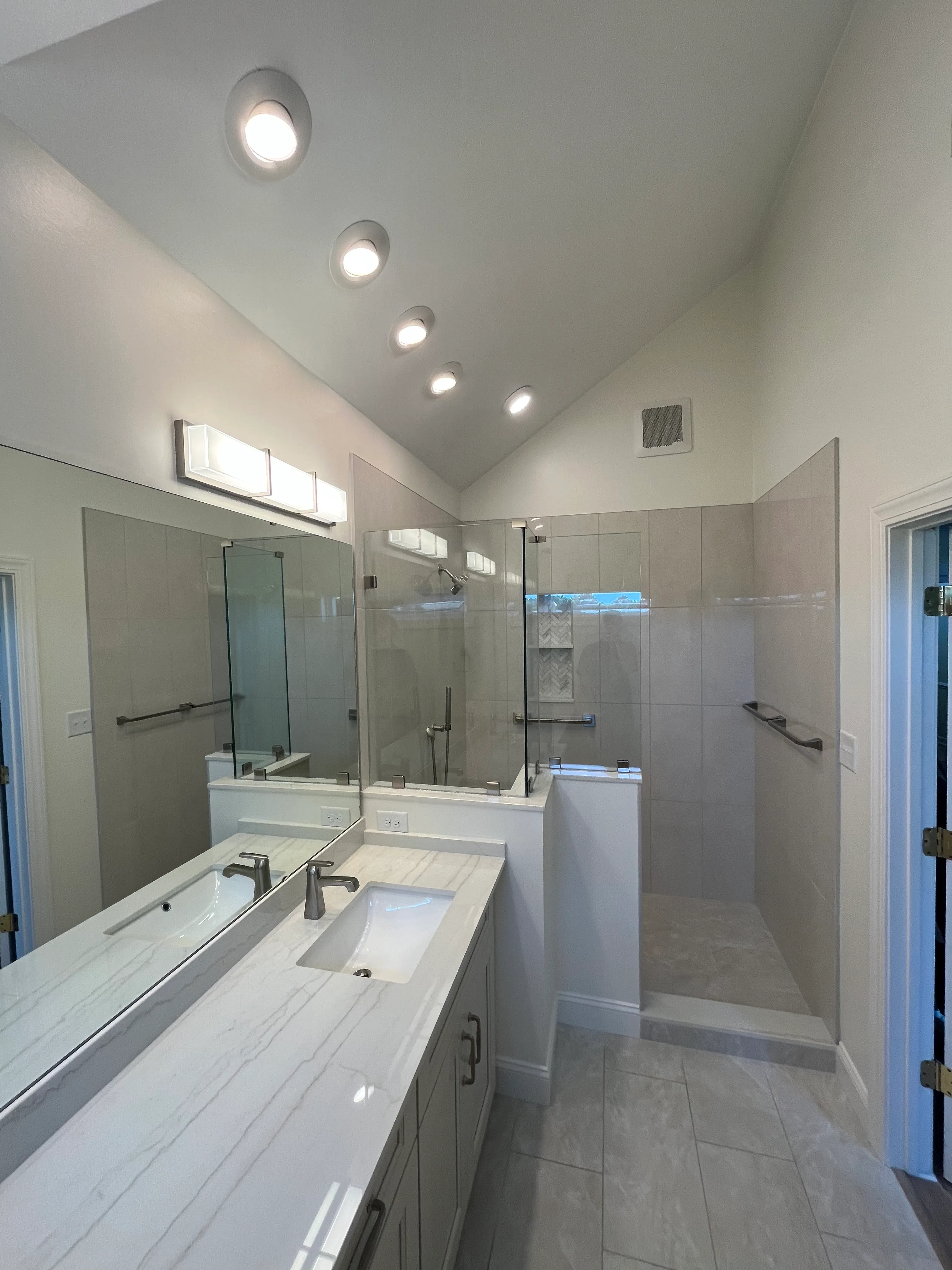Modern bathroom with white vanity, single sink, large mirror, and glass-enclosed tiled shower.