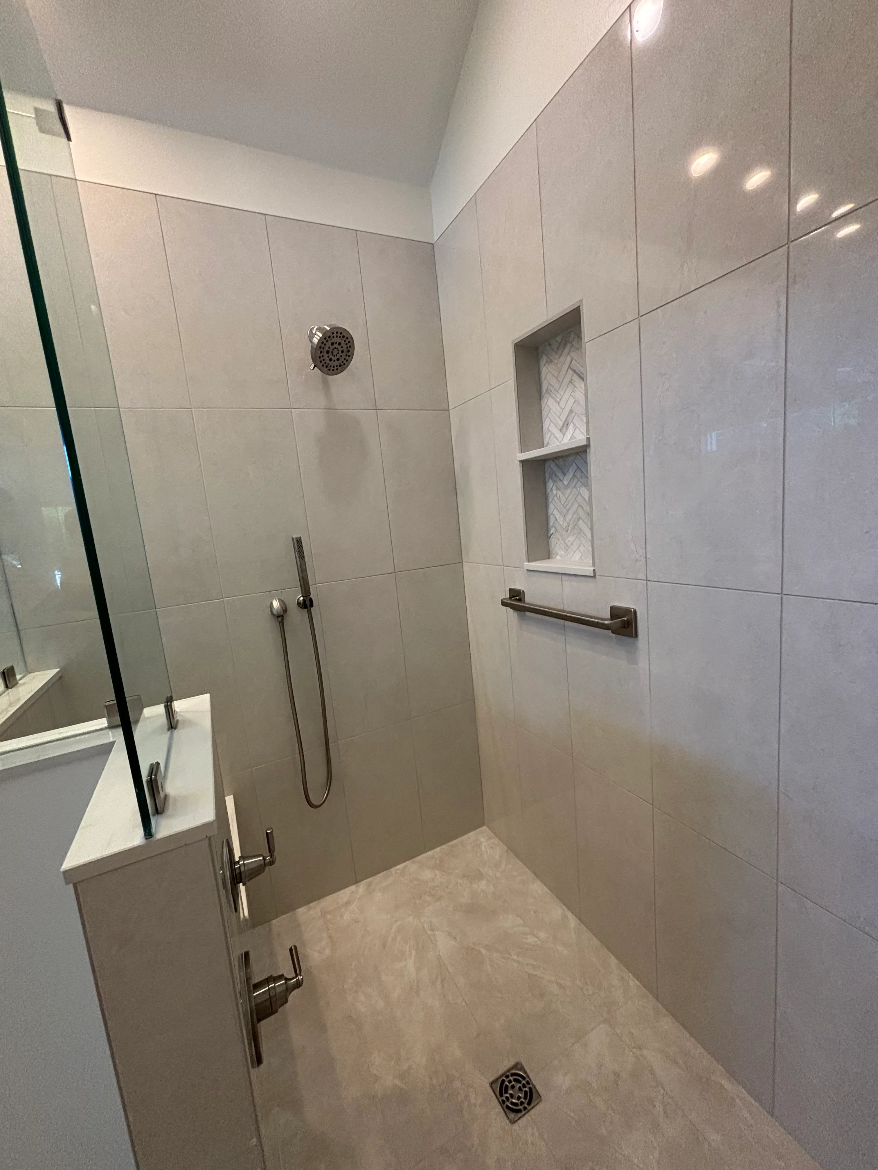 Modern tiled walk-in shower with handheld showerhead, wall niche, and metal grab bar.