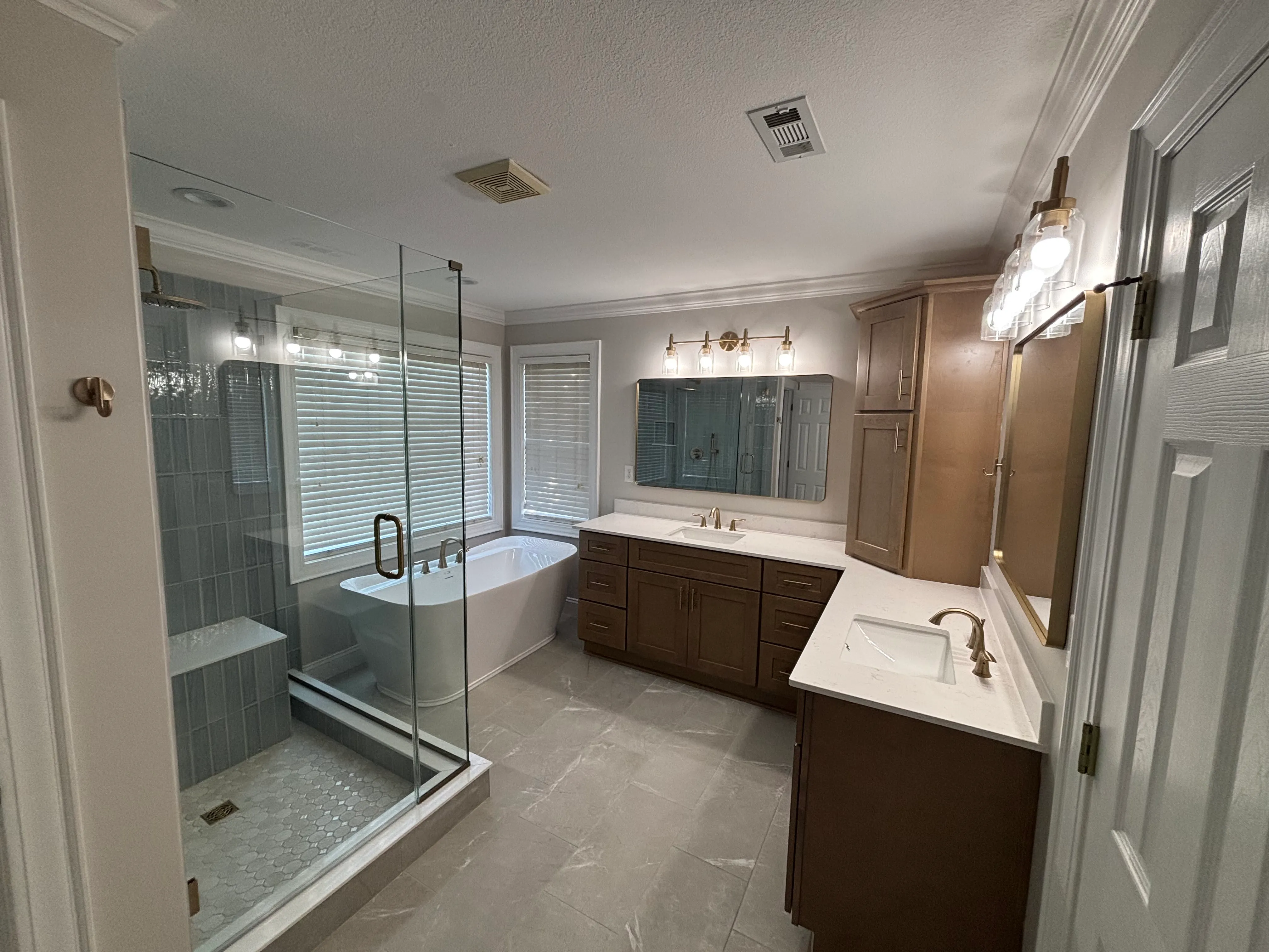Modern bathroom with glass shower, freestanding bathtub, dual sinks, wood cabinets, and large mirrors.