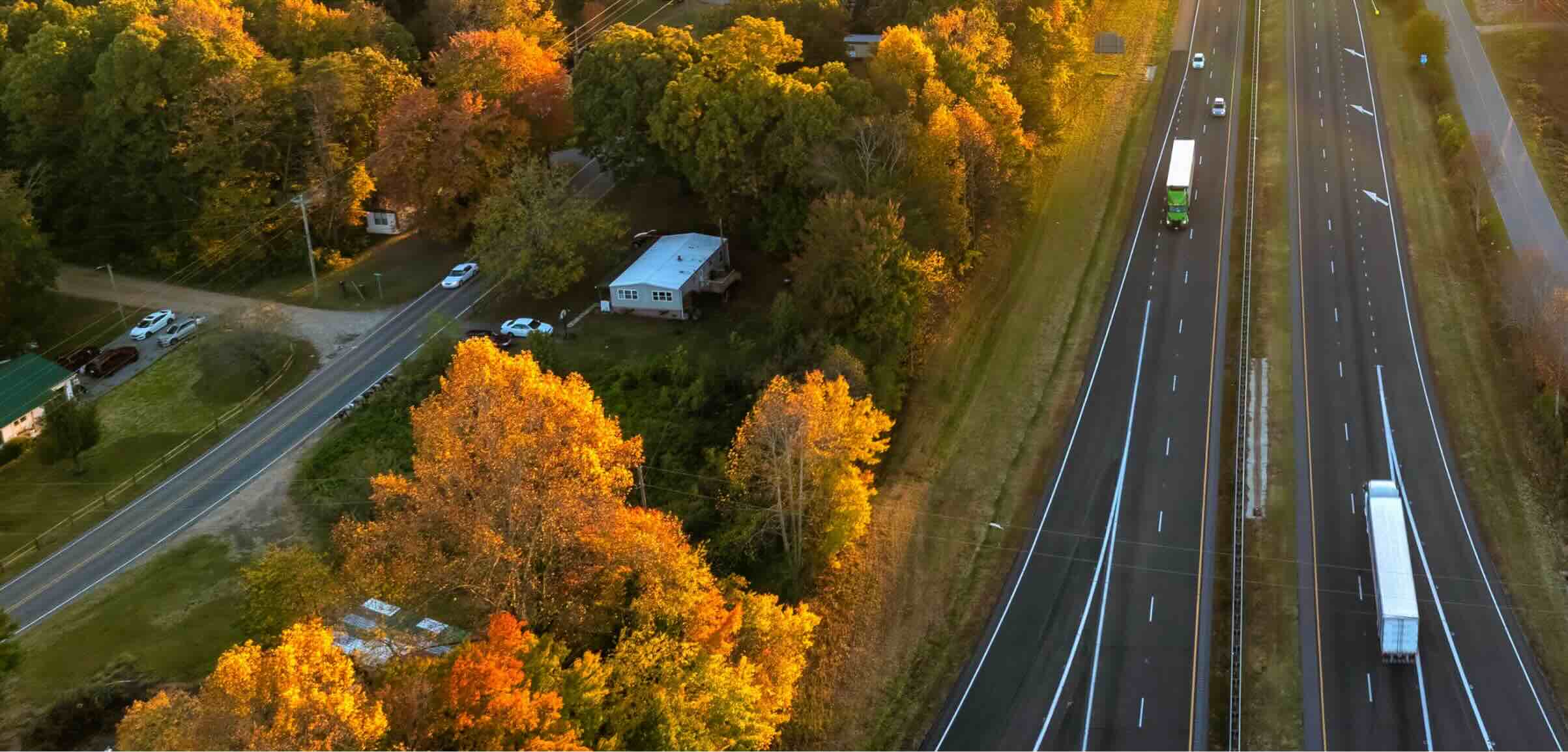 An aerial view of a peaceful landscape showcasing a two-lane highway bordered by vibrant autumn trees in shades of orange and yellow