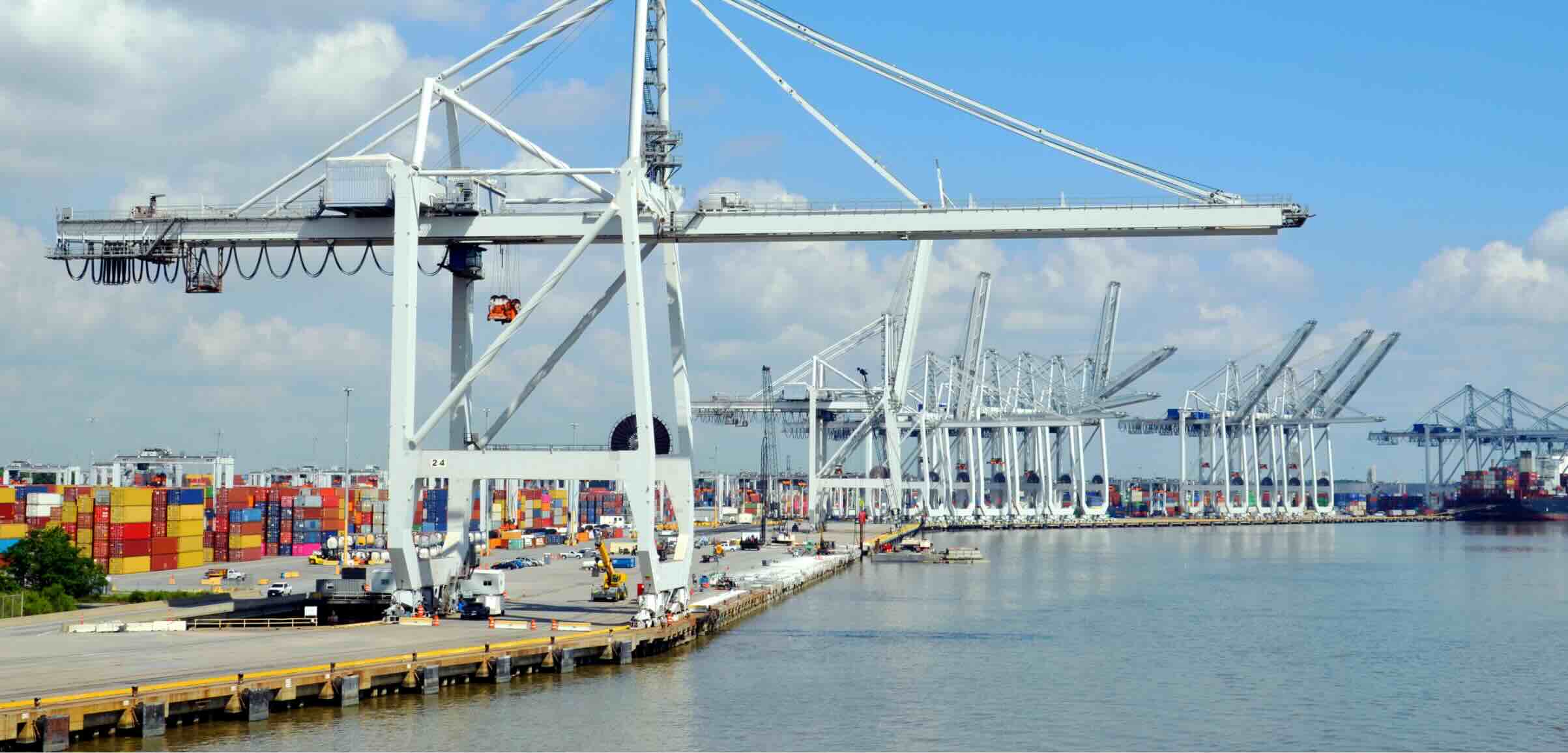 A bustling shipping port featuring large loading cranes and colorful stacked containers along the waterfront