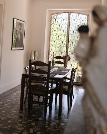Salle à manger de la maison Le Chant du Champ avec sol en terrazzo d'origine, mobilier vintage en bois et grande porte vitrée en fer forgé.