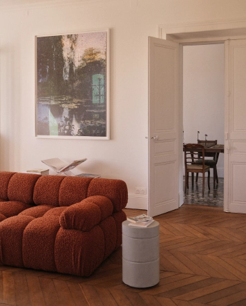 Salon de la maison de vacances Le Chant du Champ à Griselles, avec parquet en point de Hongrie, canapé design en laine bouclée terracotta et grand tableau contemporain.