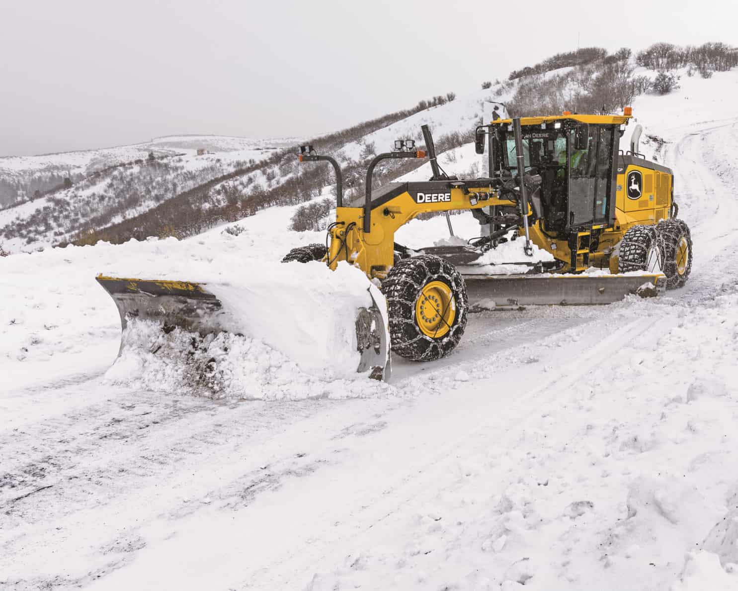 Motor grader clearing heavy snow accumulation from a large commercial lot