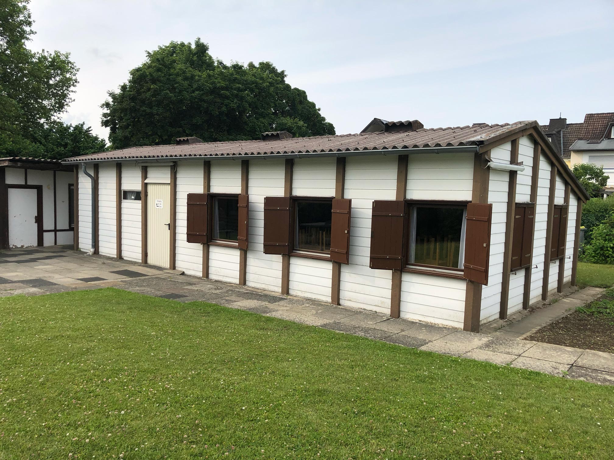 ein älteres Vereinshaus eines Kleingartenvereins im Fachwerkstil aus braunen Holzbalken und weißen Holzlatten, viele kleinere Fenster mit braunen Fensterläden