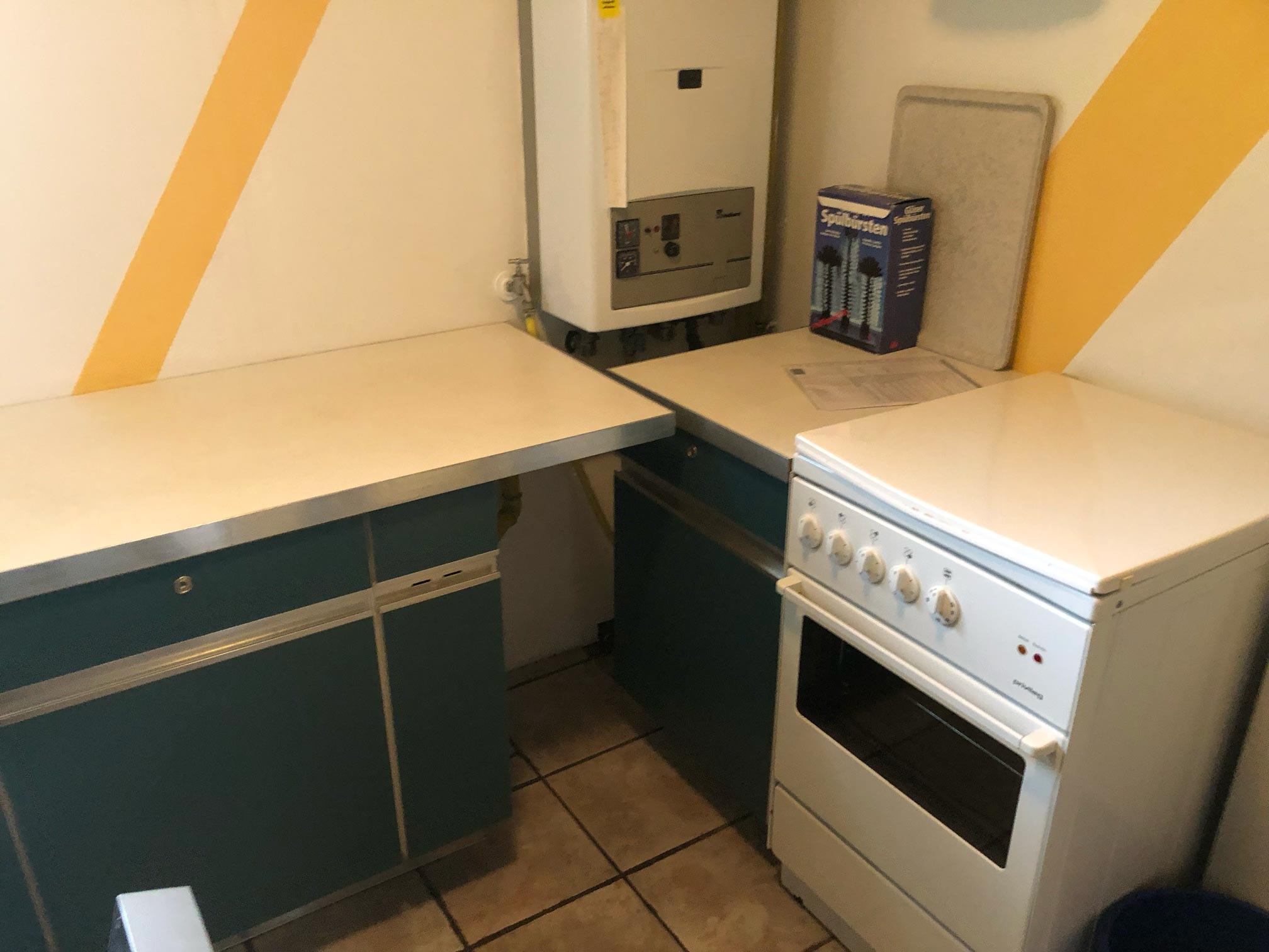 Ansicht auf die Küche mit türkisfarbenen Fronten, der Backofen und ein Heizkasten sind zu sehen