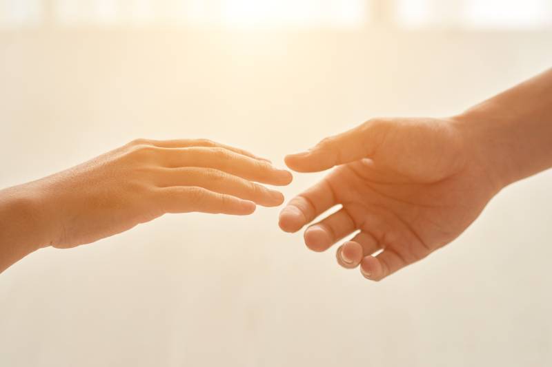Deux mains tendues l’une vers l’autre dans une lumière douce et chaleureuse.