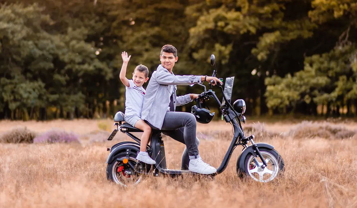 2 kinderen zitten op een fatbike. Ze staan in een droog weiland in het bos.