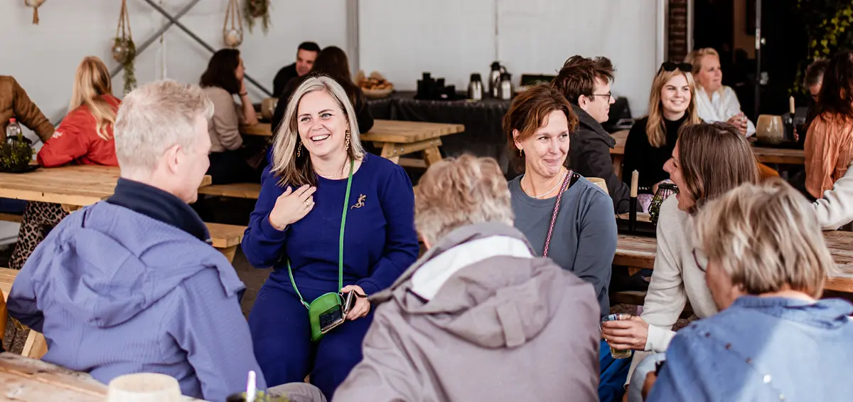 Een aantal mensen die in een tent zitten. Ze zijn met elkaar aan het praten en wachten op wat ze gaan doen.
