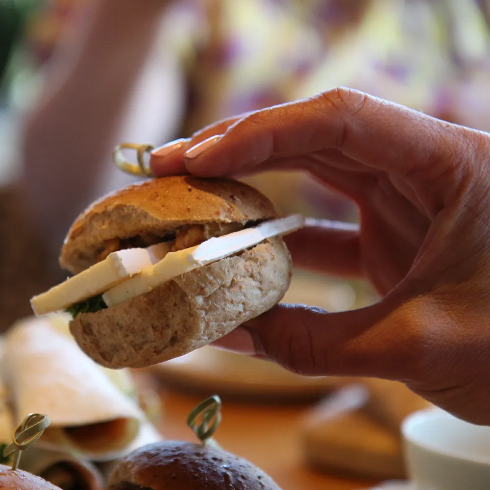 Hand houdt een klein broodje met plakjes kaas en walnoten.