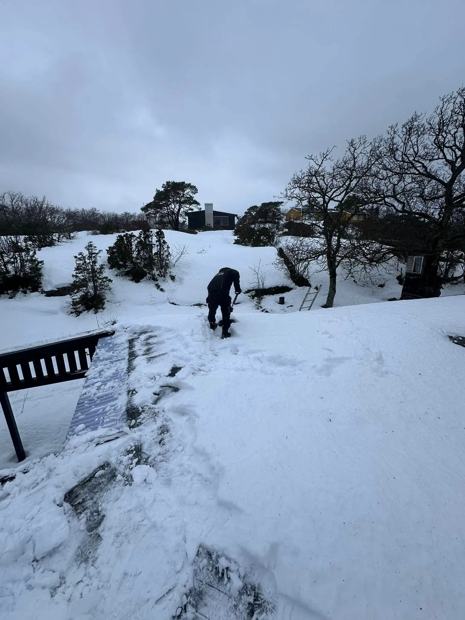 Mann som måker snø på et tak.