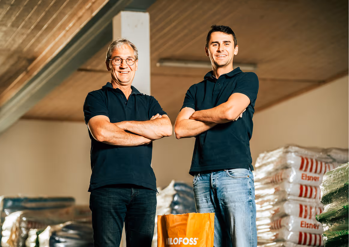 Johannes und Thomas Elsner stehen im Lager vor Futtermitteln und lachen in die Kamera