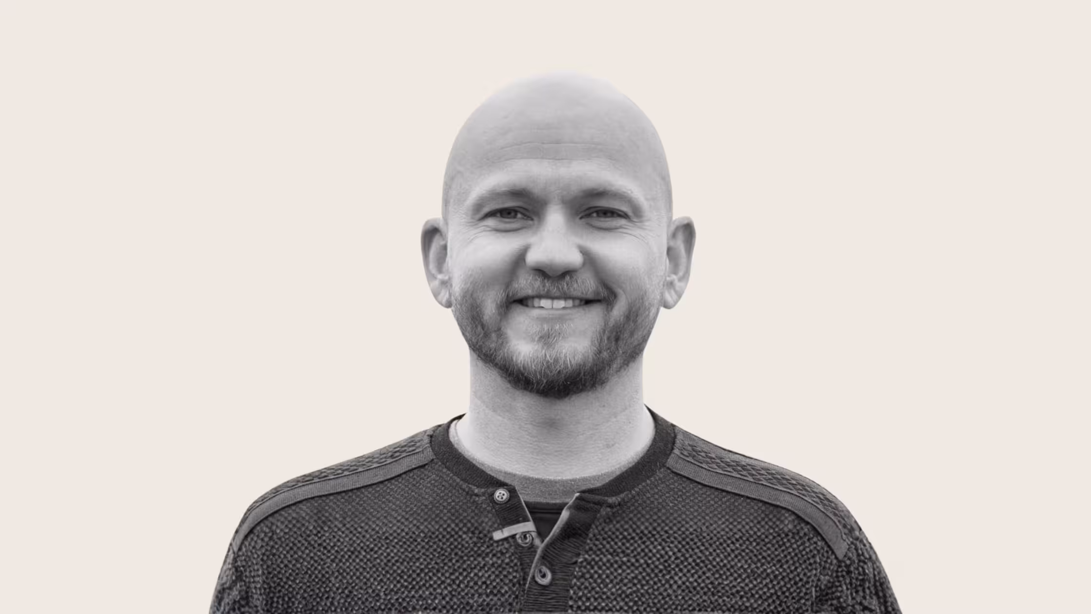 Smiling bald man with a short beard in a textured button-up sweater against a plain background.