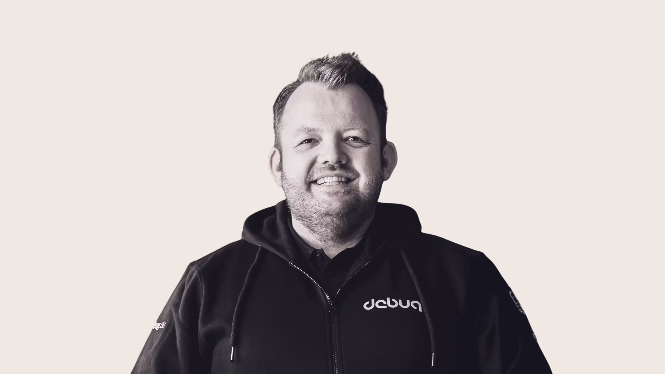 Smiling man with short hair and beard wearing a black hoodie with debug text on it.