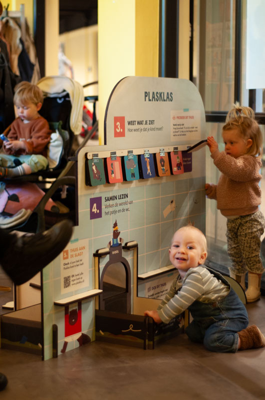 Lachende peuter ligt op de grond en speelt met een uitgevouwen boek over zindelijkheid