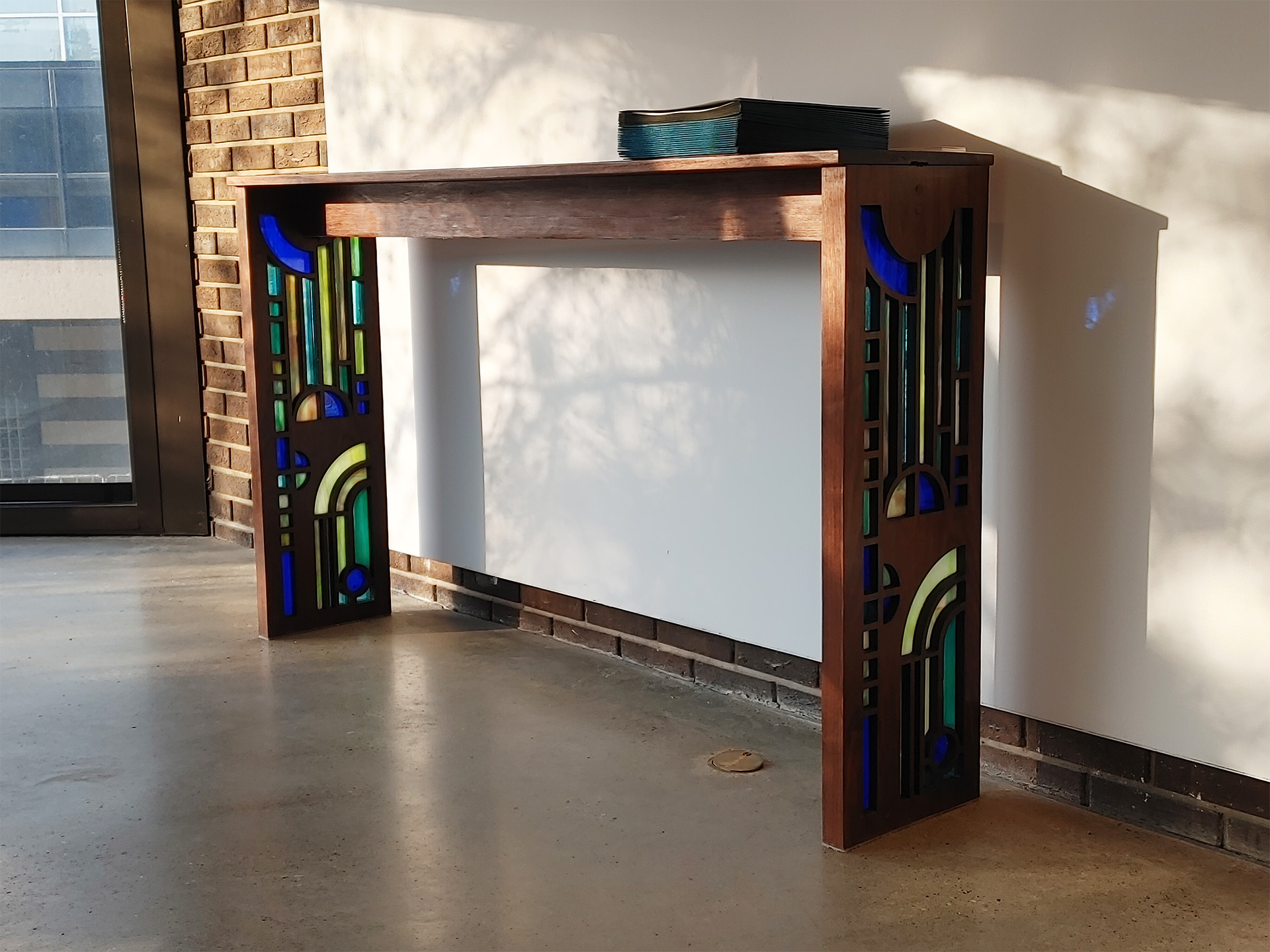 Photo of the table from a further angle, showing it against the wall in a gallery, lit from the left.