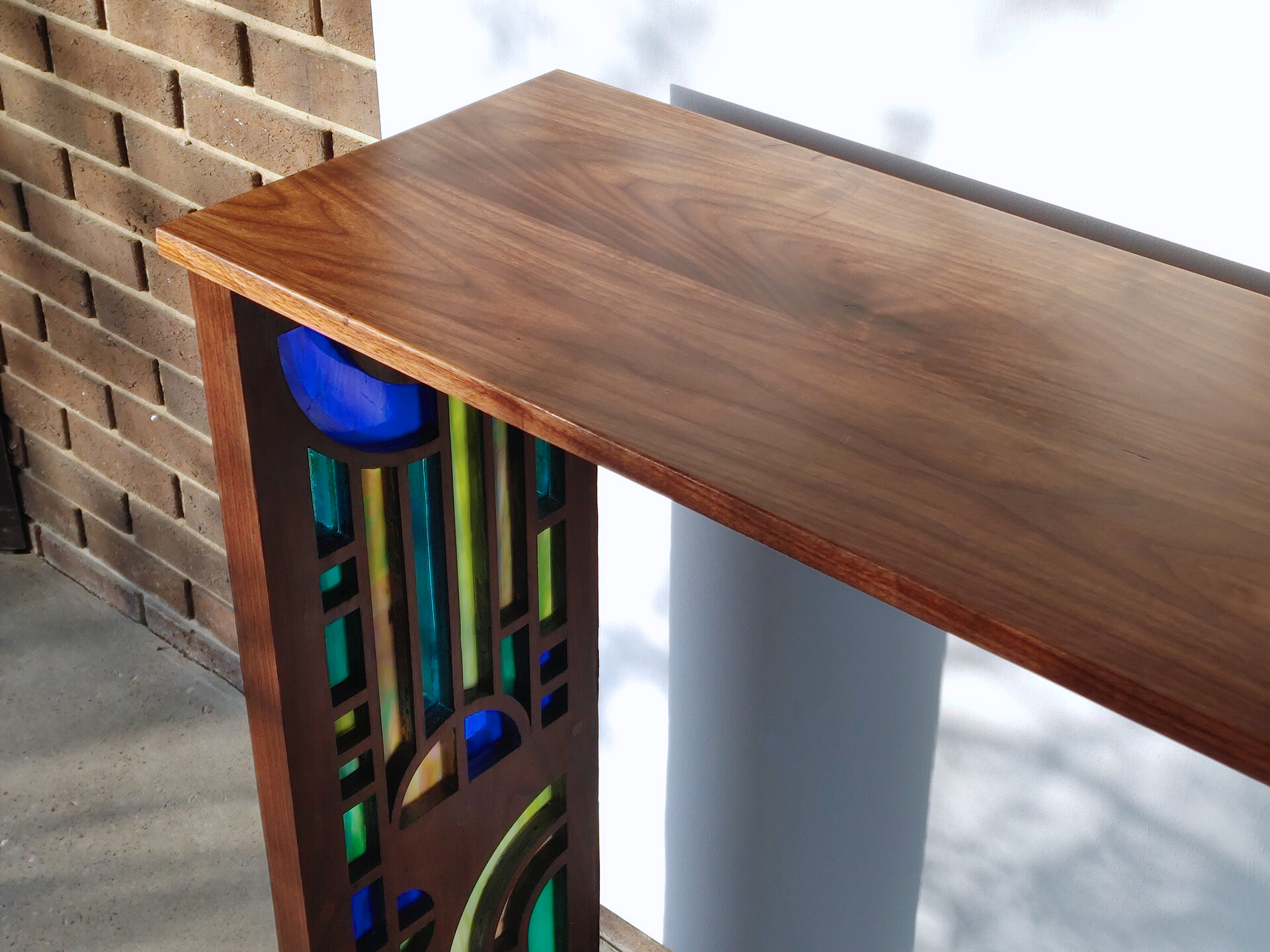 Thumbnail image of the "Wright Console Table". The photo of the table is taken at an angle to show the wood grain of the walnut tabletop, at a diagonal with the legs, which have pieces of blue, green and multicolor stained glass inlaid.