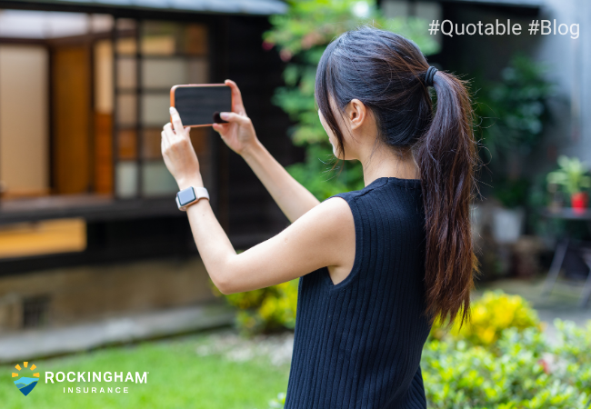 Homeowner using a smartphone to photograph a house exterior as part of a home insurance property inspection.
